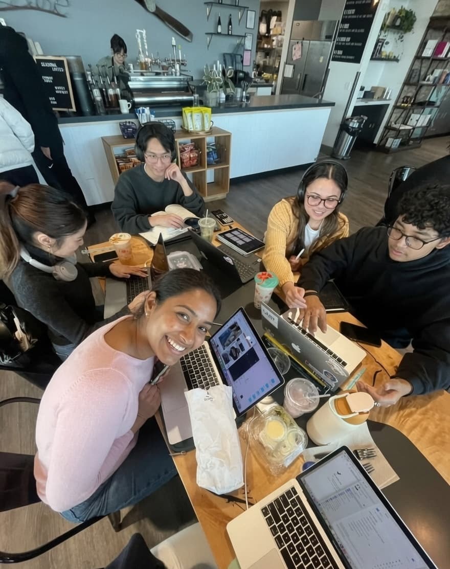A group of students collaborating around a table on laptops at a coffee shop